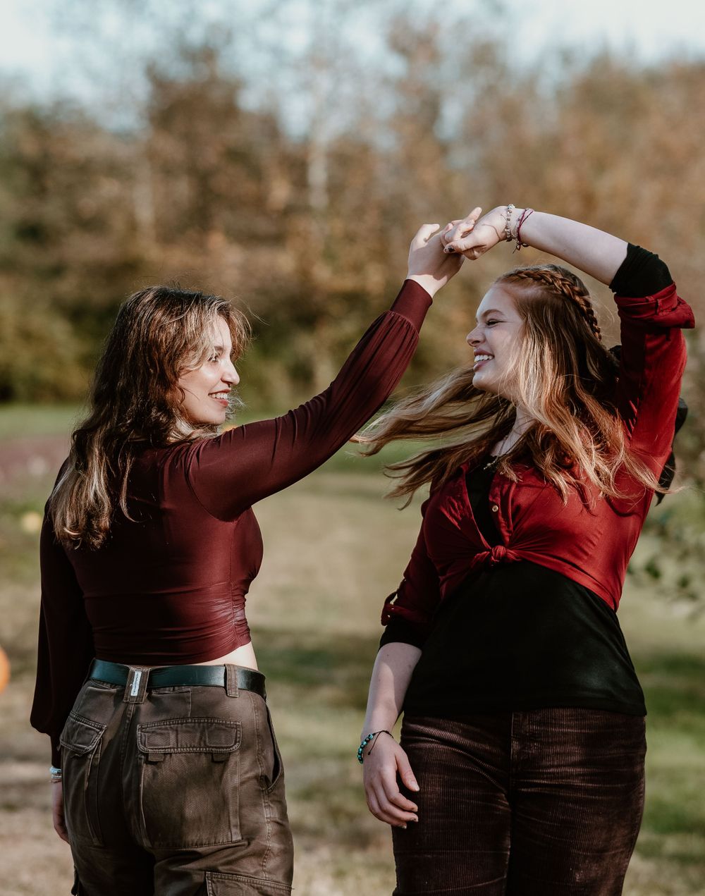 Two people in burgundy tops dancing and twirling together outdoors.