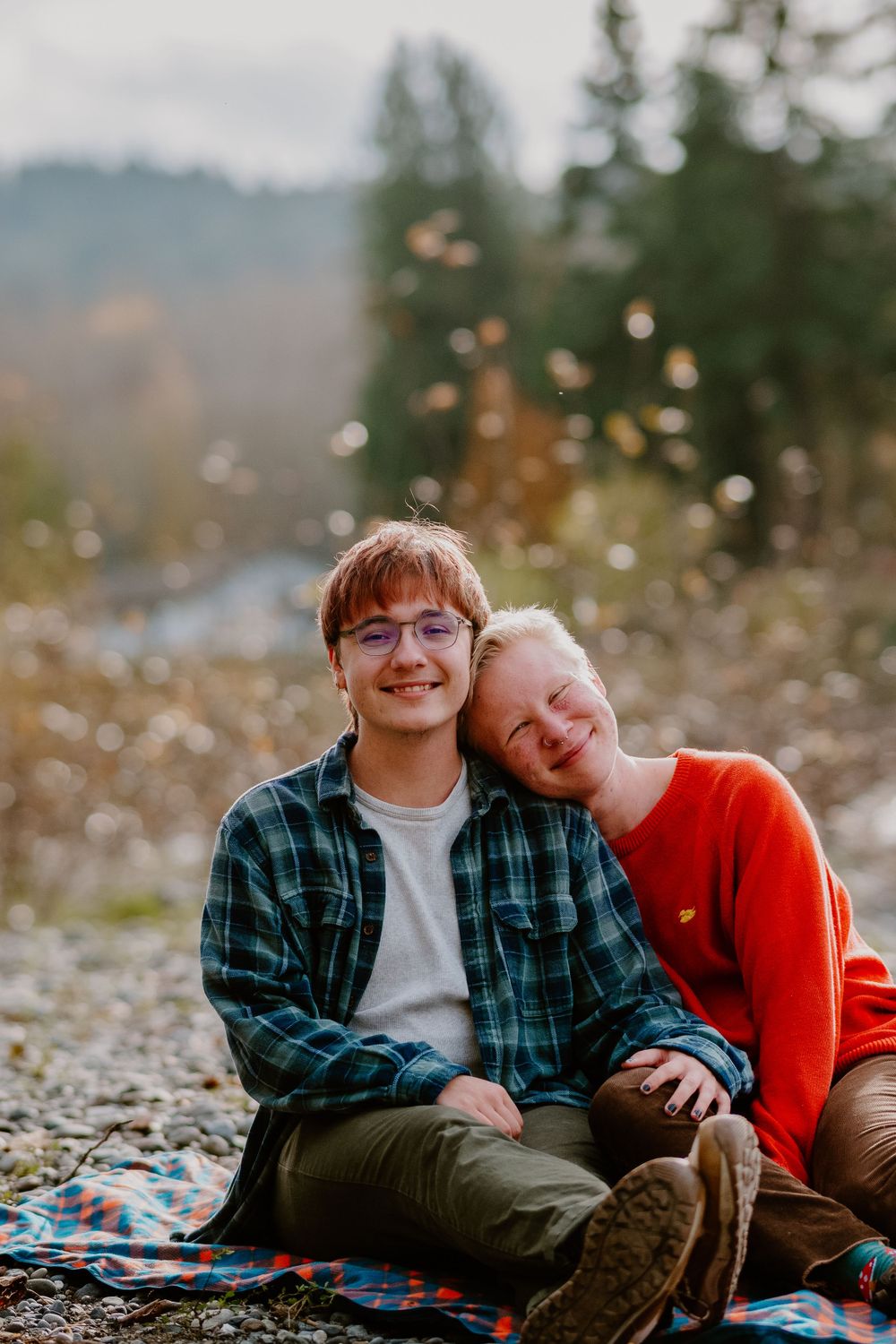 A couple sitting close together on a blanket with sparkly bokeh lights in the background.