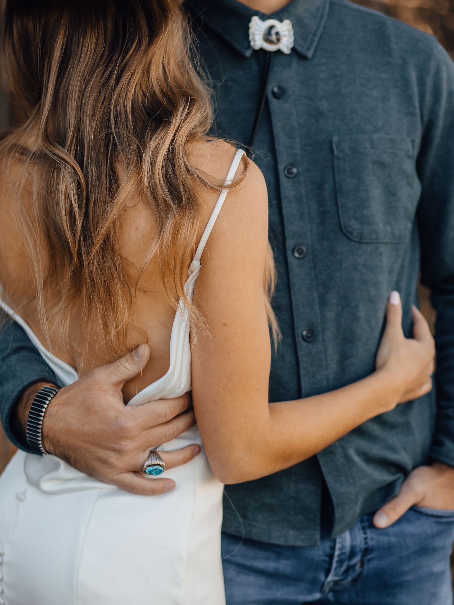 Couple in casual denim and white embracing showing turquoise ring detail.
