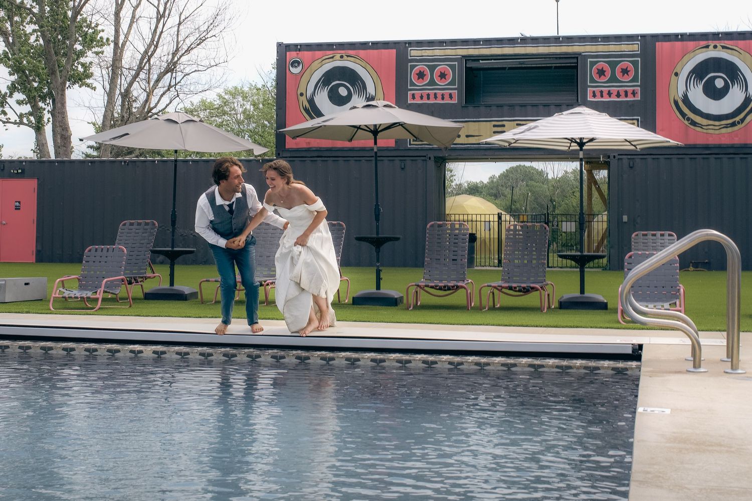 Bride and groom dancing by a pool at an outdoor wedding venue with a colorful DJ booth backdrop.