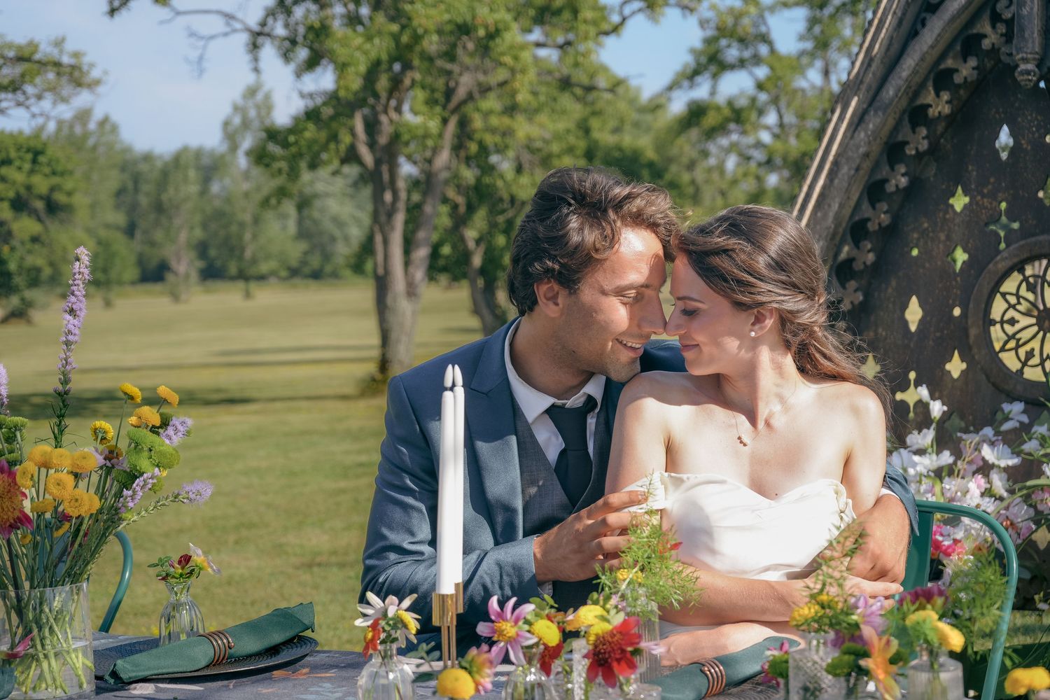Couple sharing a romantic moment at a floral-decorated outdoor wedding table surrounded by colorful wildflowers.