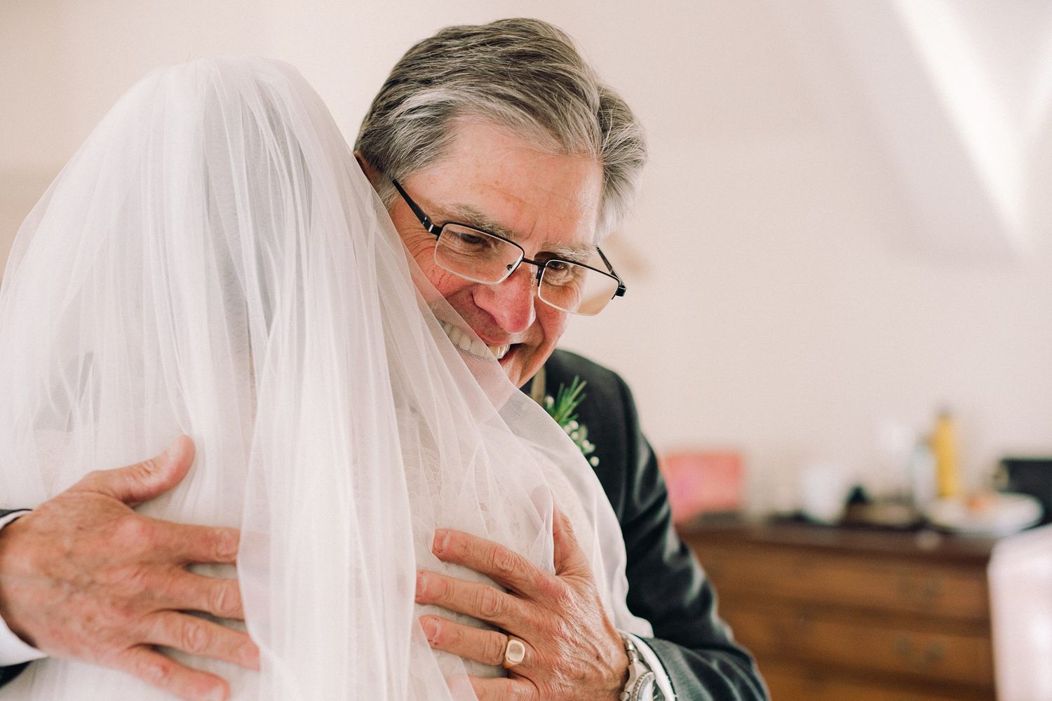 Father embracing bride in wedding veil during emotional pre-ceremony moment.