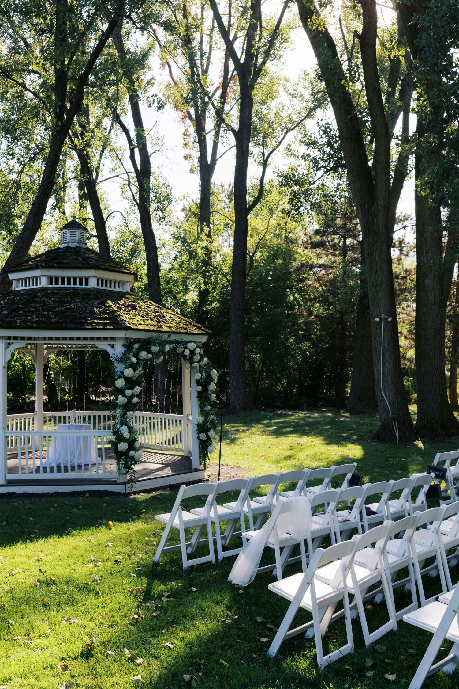 Outdoor wedding ceremony setup at the Abbey Resort, white chairs facing a decorated gazebo surrounded by tall trees on a lush green lawn.