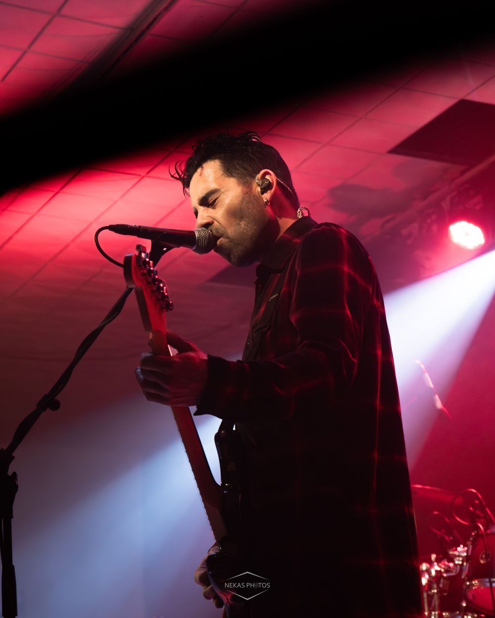 Male guitarist performing on stage under red and blue lights, playing a red electric guitar at a live concert.