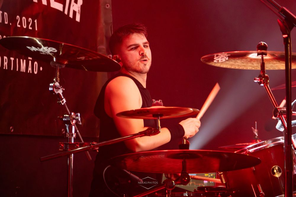 Young male drummer playing drums on stage under red lighting at a live concert in 2021.