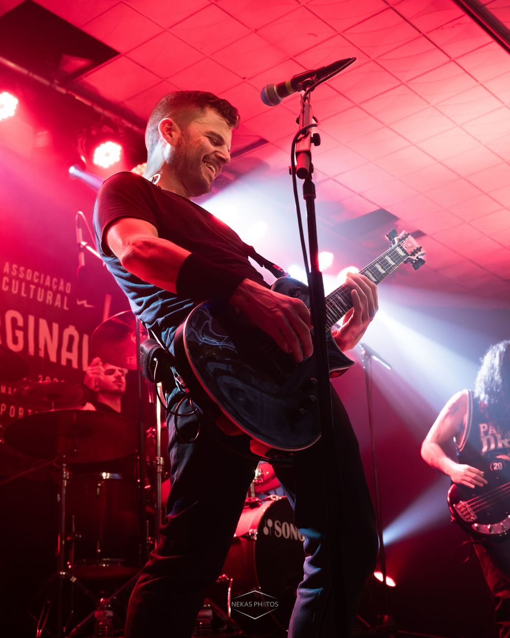 Guitarist performing on stage under red lights at a live rock concert venue.
