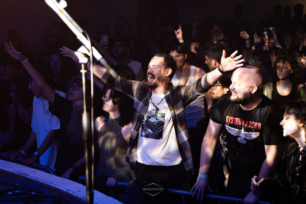 Two men on stage with hands raised, engaging an energetic crowd at a live music concert event.