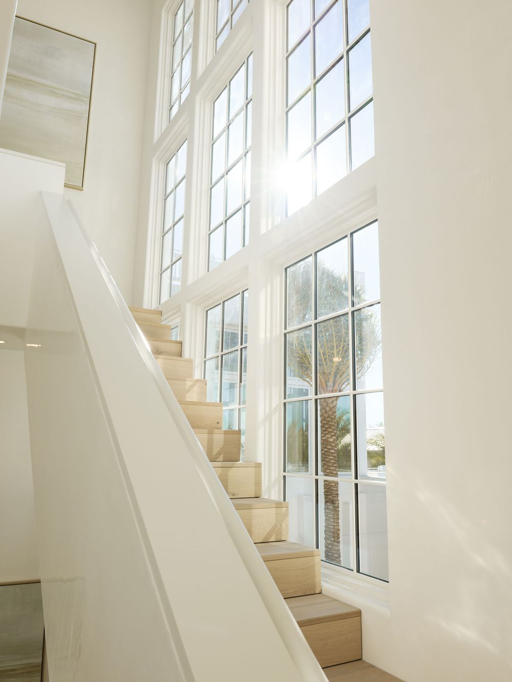 Bright white staircase with natural wood steps beside tall grid windows flooding the space with sunlight.