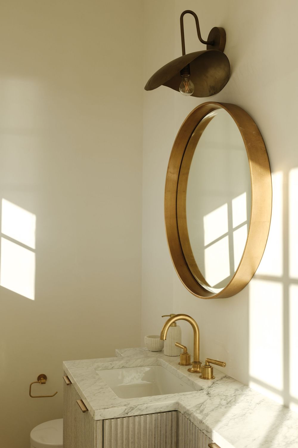 Elegant powder room with marble vanity, brass fixtures, round gold mirror, and antique wall sconce.