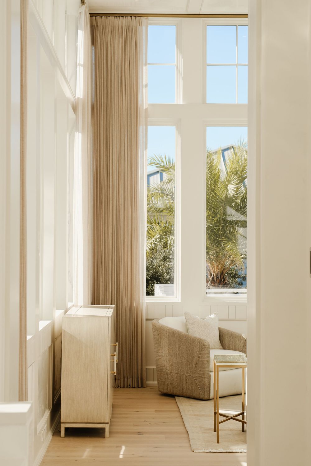 Elegant living room with tall arched windows, linen curtains, and neutral furnishings.