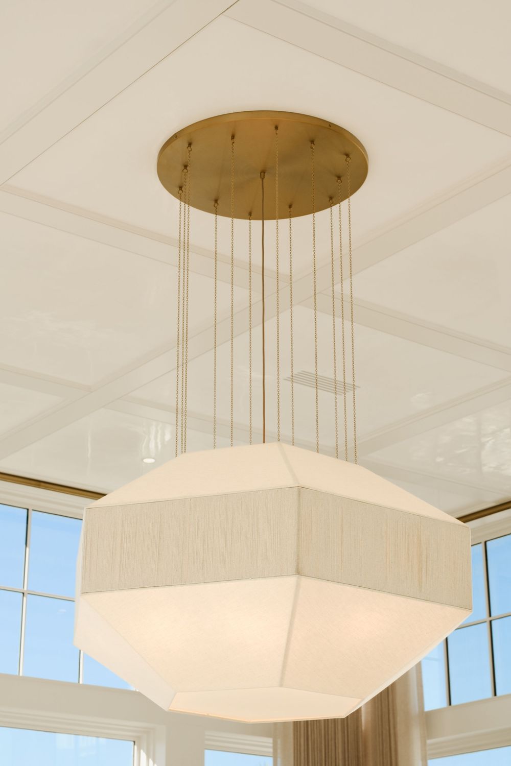 Elegant geometric white pendant light fixture with brass ceiling mount in a bright modern living space.