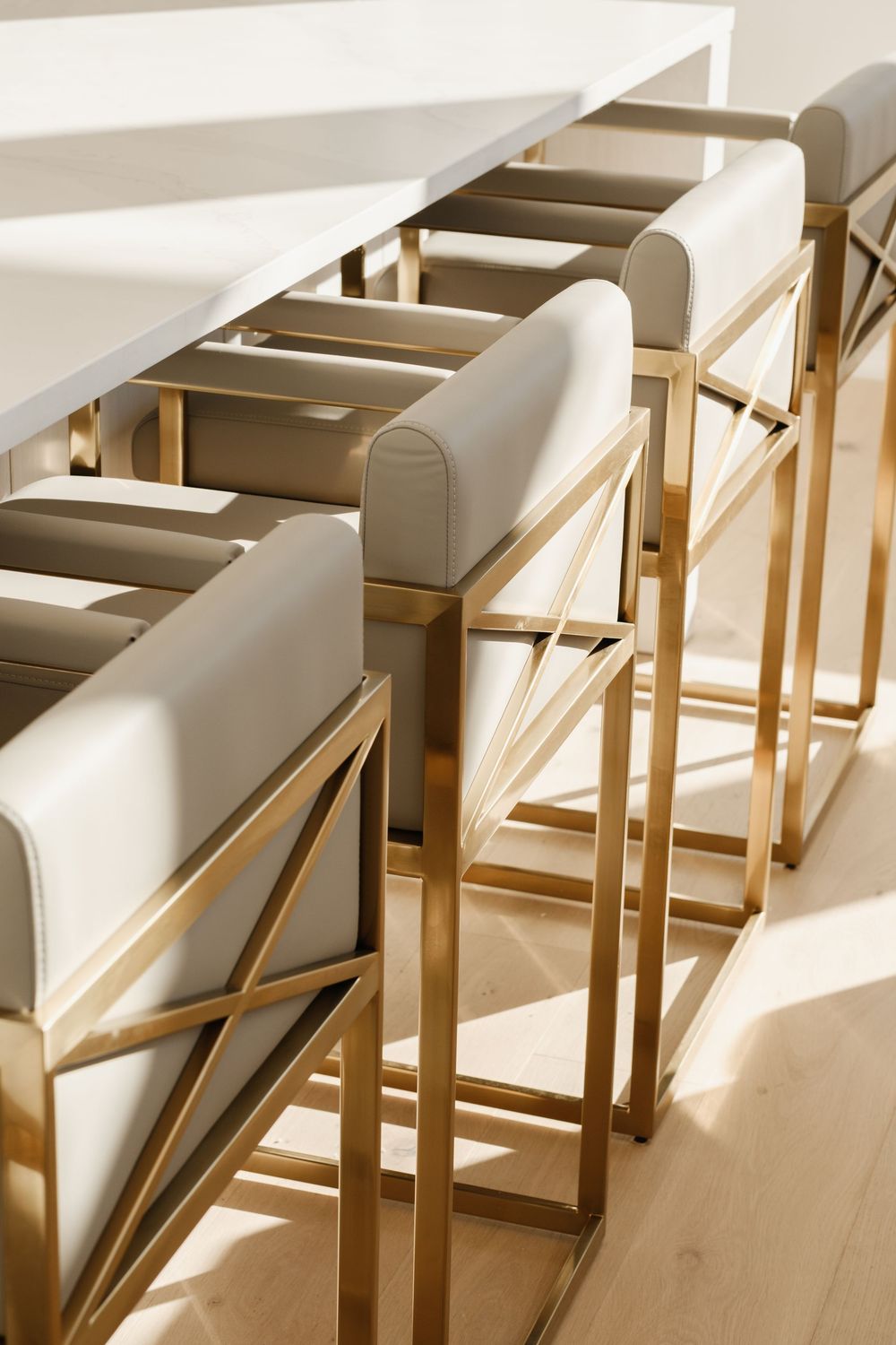 Modern gold bar stools with white cushions lined along a marble kitchen island.