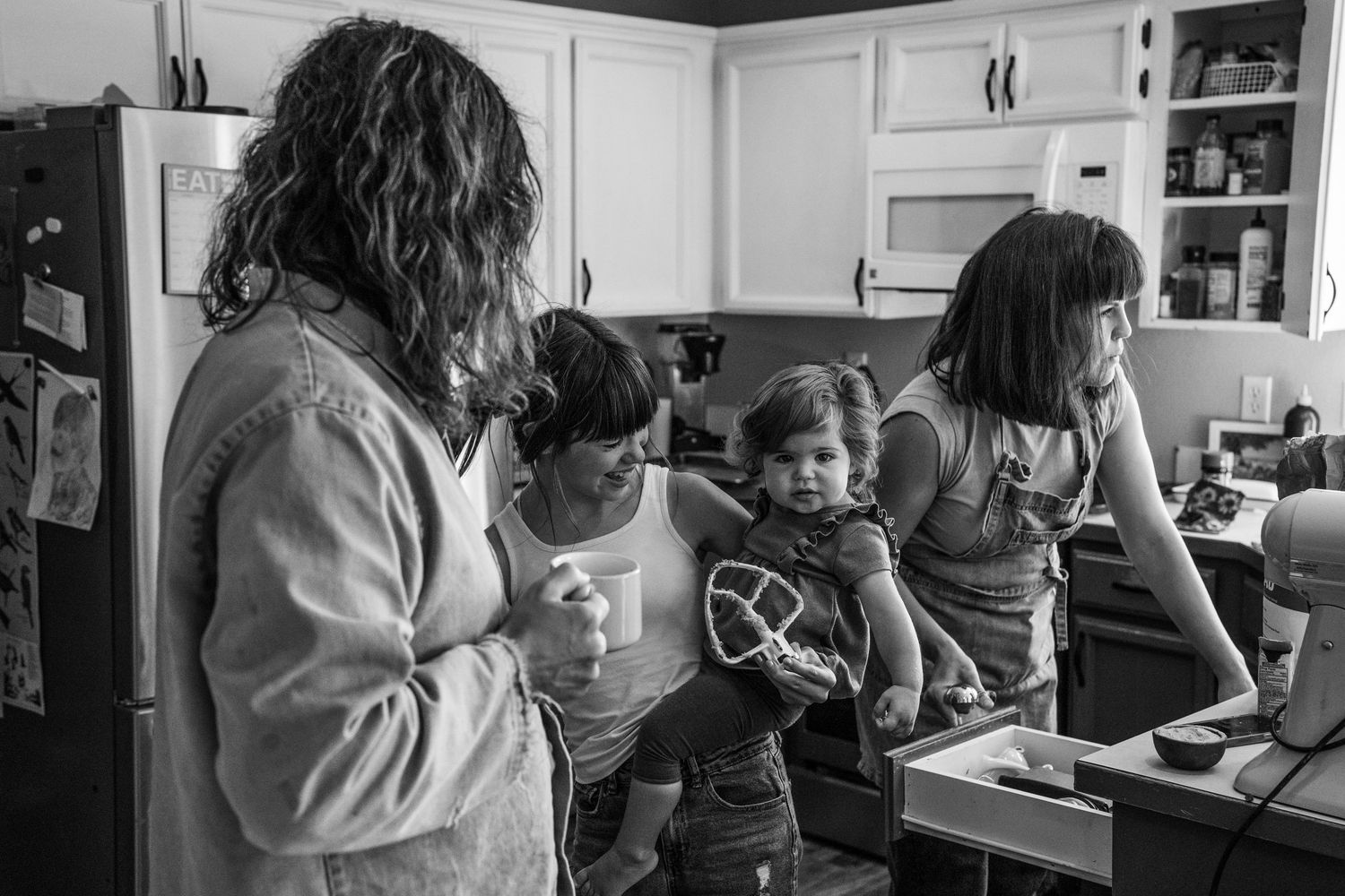 Black and white photo of a family with children gathered in a cozy kitchen, sharing a warm moment together.