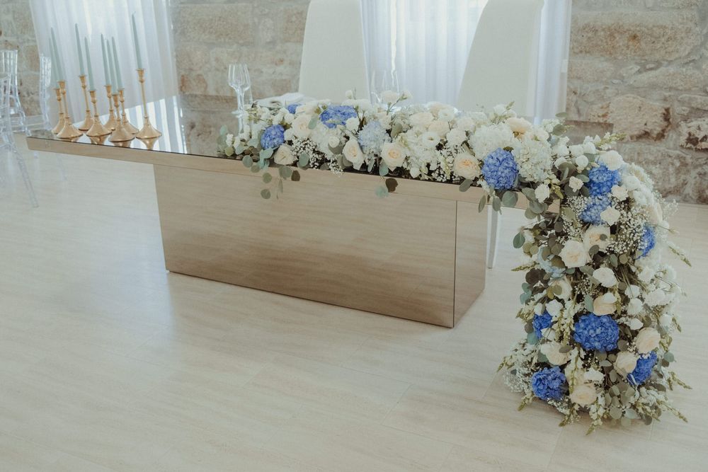 Elegant wedding table with white and blue floral arrangement featuring hydrangeas and roses on a wooden box centerpiece.
