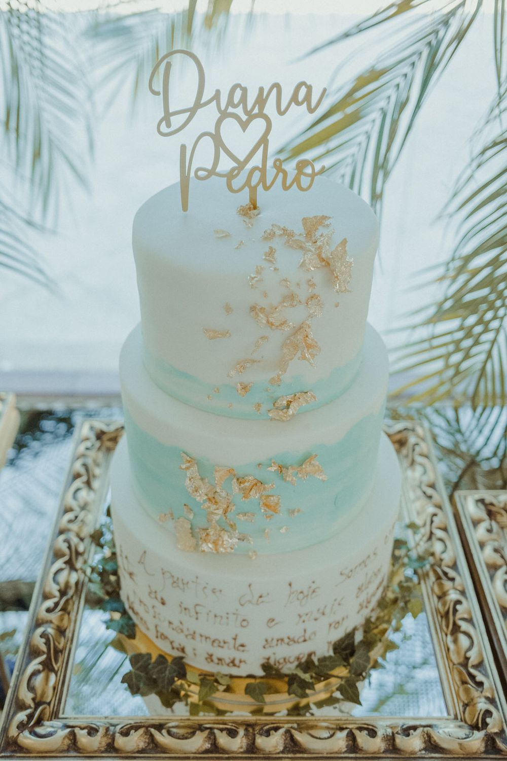Elegant three-tier mint and white wedding cake with gold leaf accents and custom Diana & Pedro cake topper.