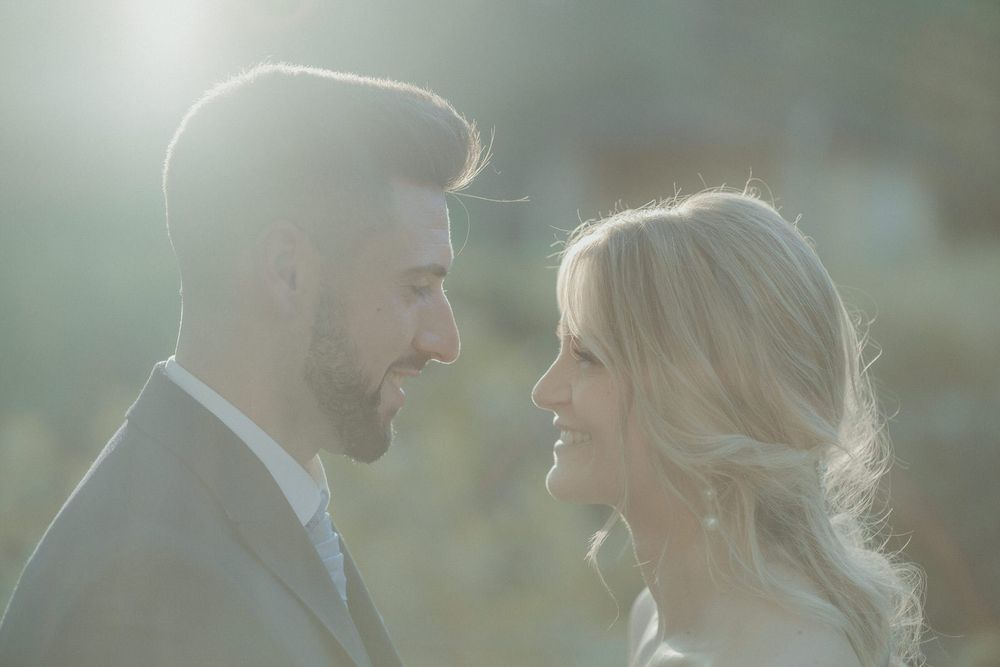 Bride and groom share a romantic moment in soft golden sunlight, gazing lovingly at each other outdoors.