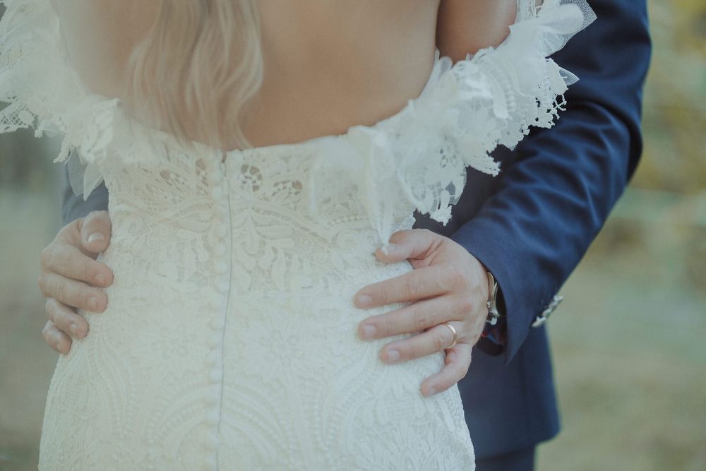 Groom in navy suit tenderly holds brides waist in lace wedding dress during romantic outdoor ceremony.
