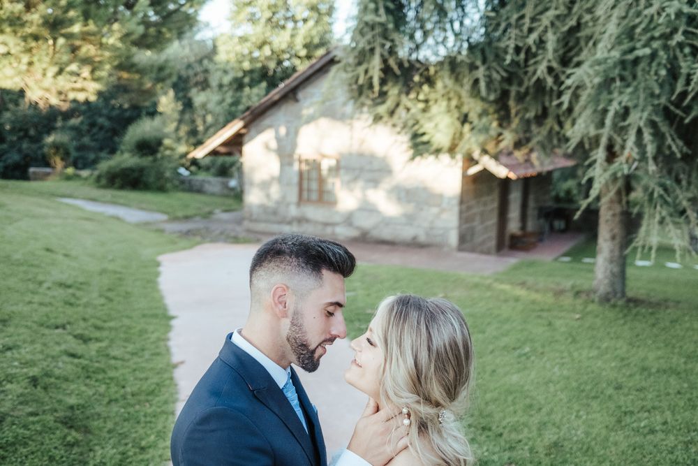 Romantic couple sharing an intimate moment outdoors near a rustic stone building surrounded by lush green trees.