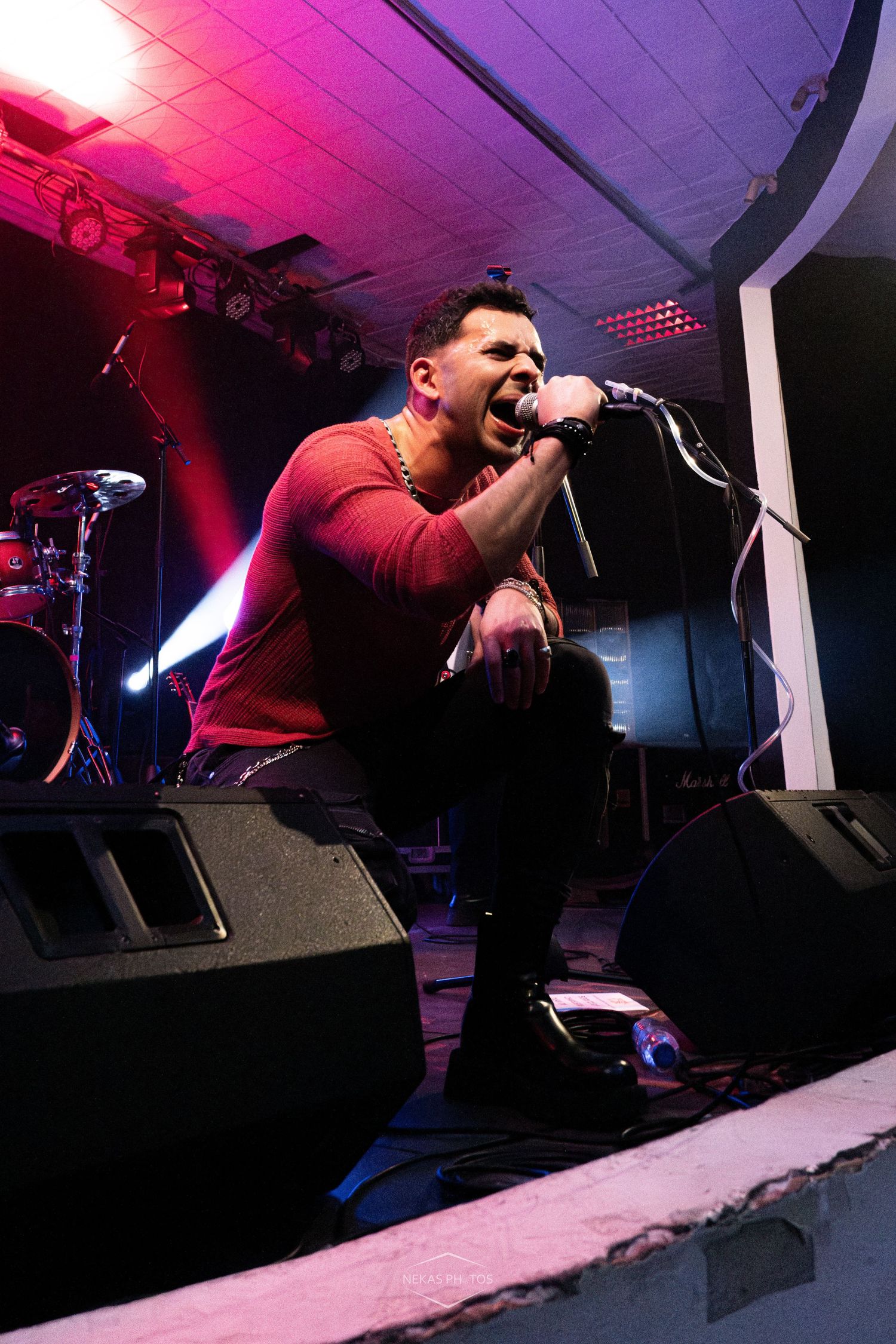 Male vocalist performing on stage, kneeling with microphone, red shirt, dramatic stage lighting.
