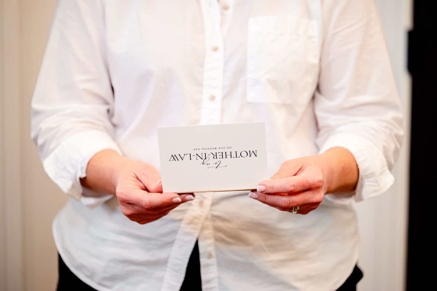 Person in white shirt holding a elegant wedding card with calligraphy text at a formal event.