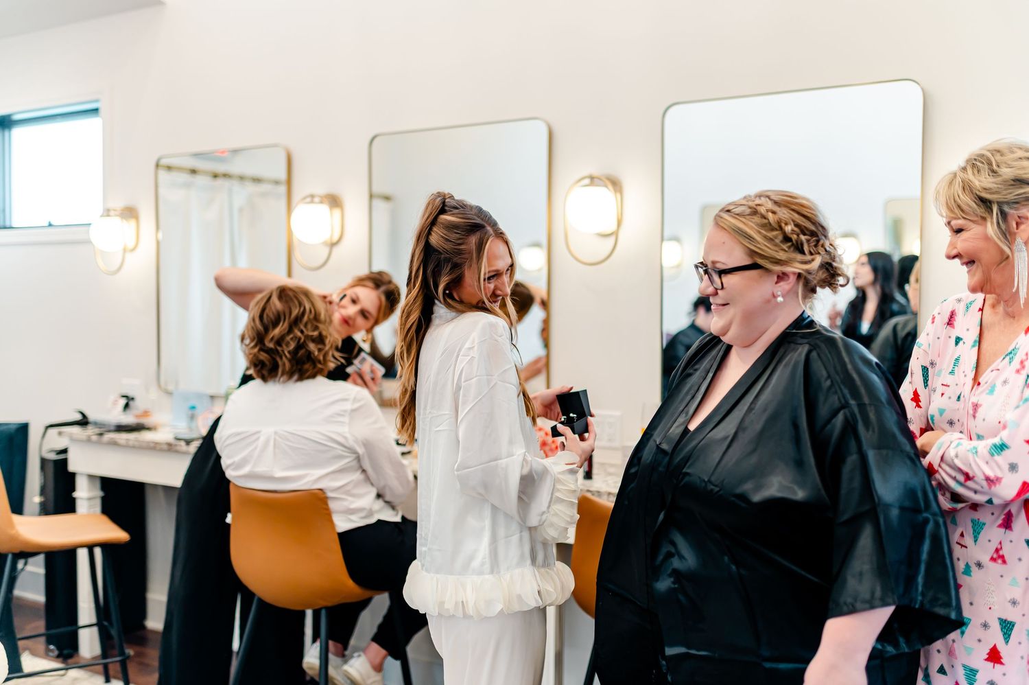 Bridal party getting ready in a salon, with makeup artists styling the bride in a white robe.