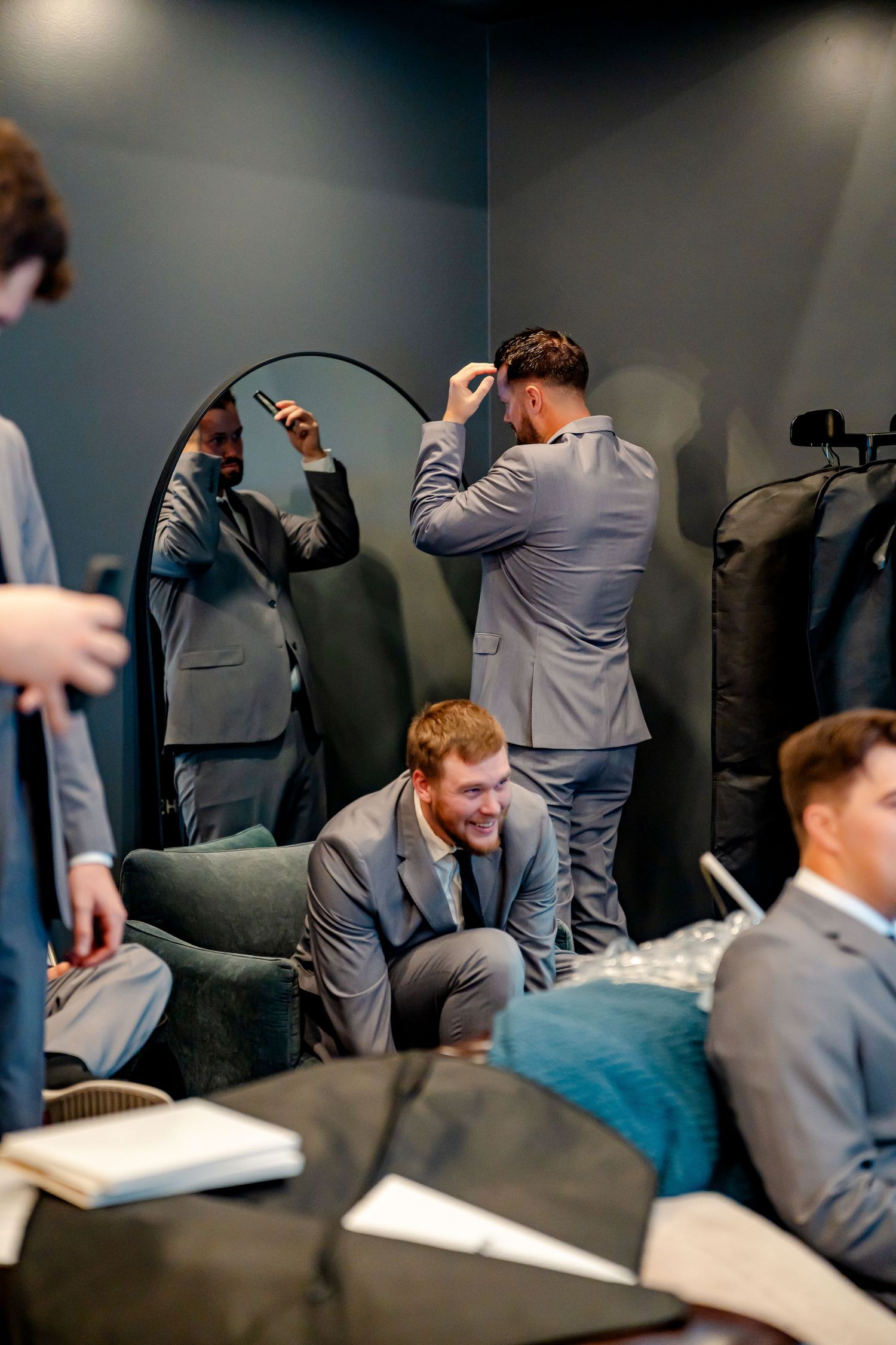 Groomsmen in gray suits laugh and prepare together in a stylish dressing room before a wedding ceremony.