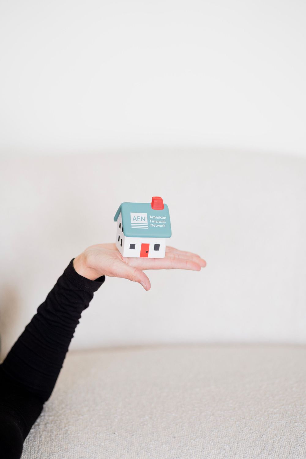 Hand holding a small AFN American Financial Network branded miniature house model.