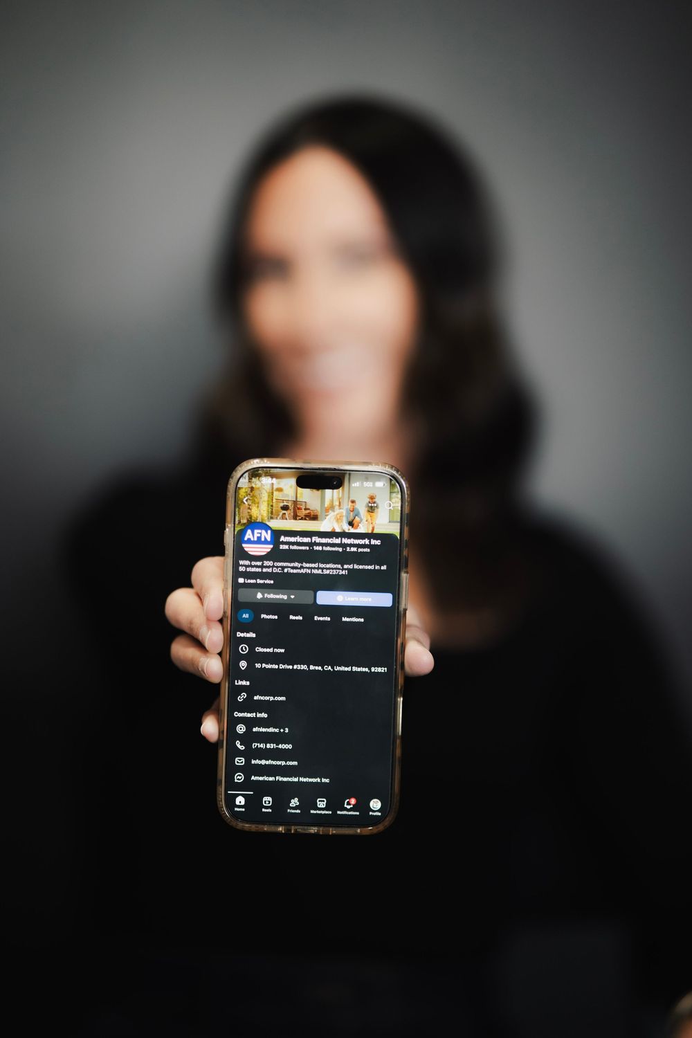 Woman holding smartphone displaying AFN American Financial Network Facebook page profile.