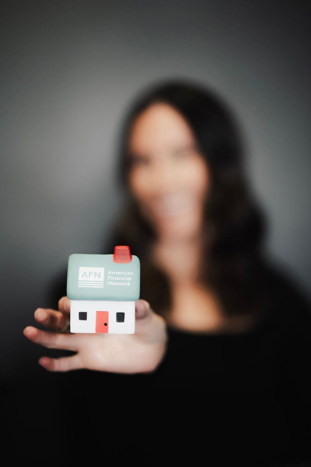Woman holding AFN American Financial Network branded miniature house toward camera, smiling.