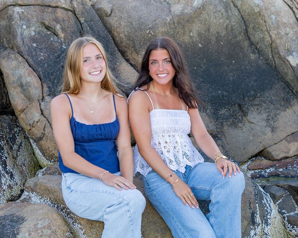 Sisters pose together on the rocks at Wingaersheek Beach in Gloucester, MA at sunset during high school senior portrait photo session.