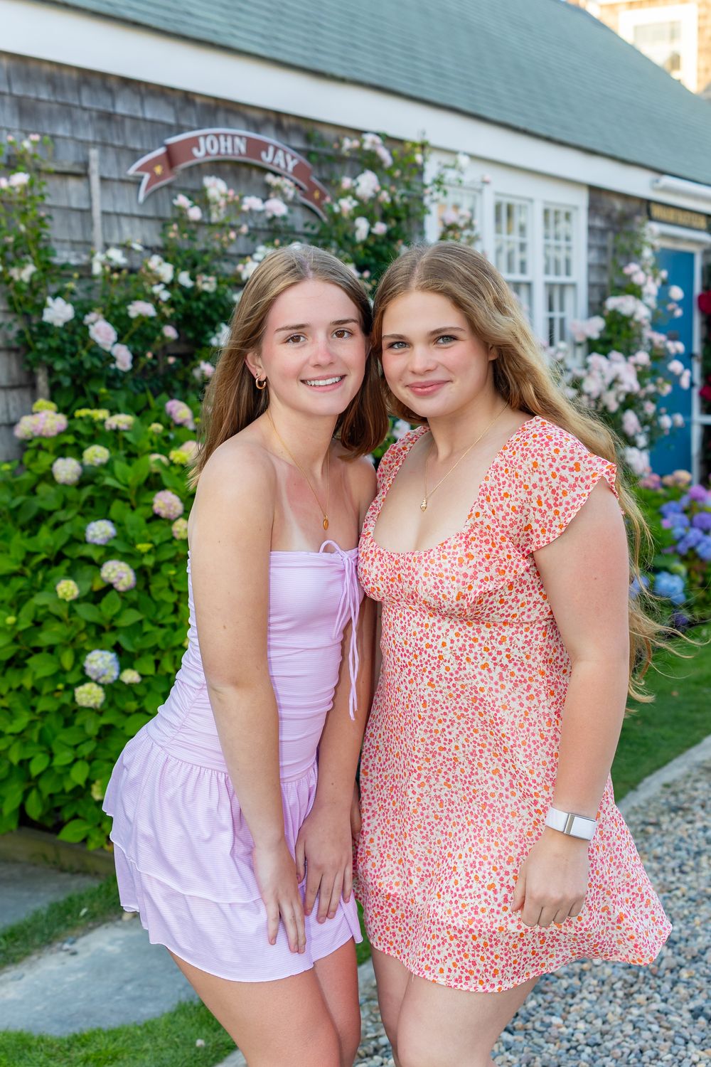 Sisters in summer dresses pose together outside a charming cottage with hydrangeas & roses on Old North Wharf on Nantucket, MA.