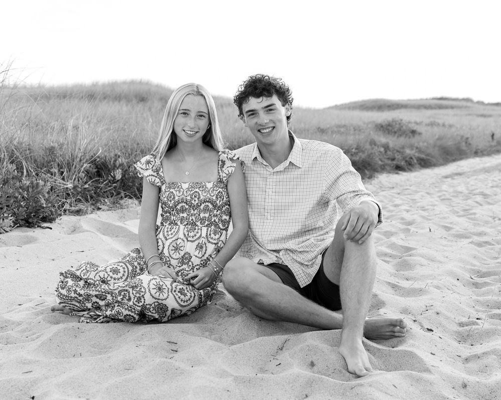 Black & white photo of two teenage siblings sitting together on sandy beach dunes during family beach photos at Miacomet on Nantucket.
