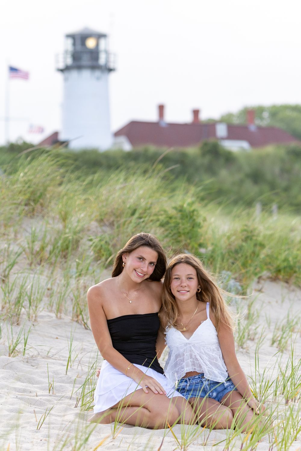 Teenage girls pose on sandy beach dunes with green grass during friend portrait session at Lighthouse Beach in Chatham, MA. Cape Cod