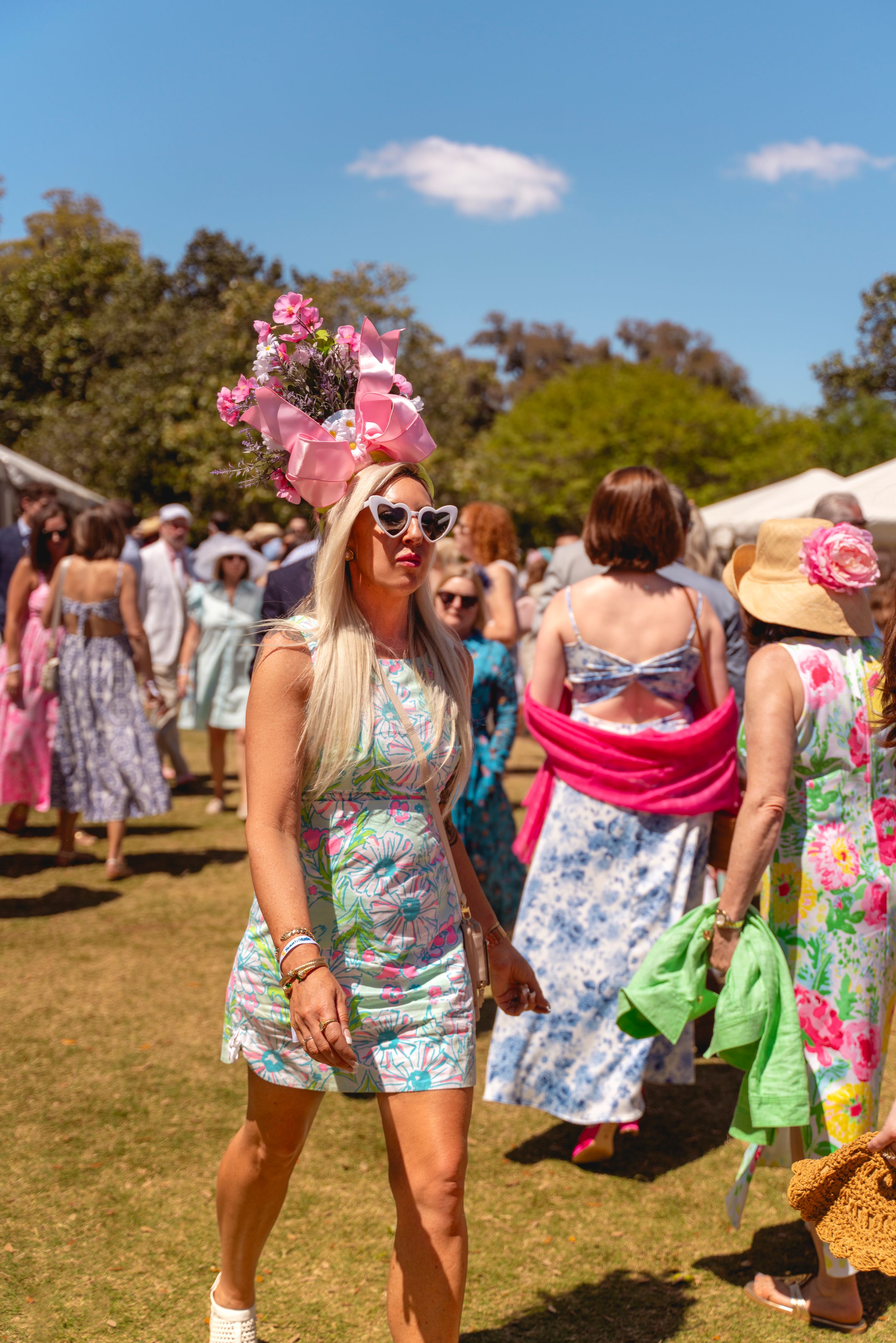 Woman in floral mini dress and pink flower fascinator hat at outdoor garden party event on sunny day.