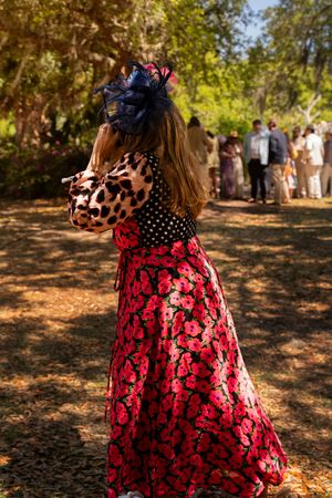 Woman in floral red skirt and leopard print top with navy fascinator at outdoor garden wedding ceremony.