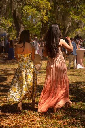 Two women in elegant floral maxi dresses walking toward outdoor garden party celebration.