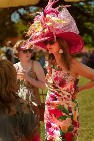Woman in floral dress and pink feathered hat at outdoor garden party event.