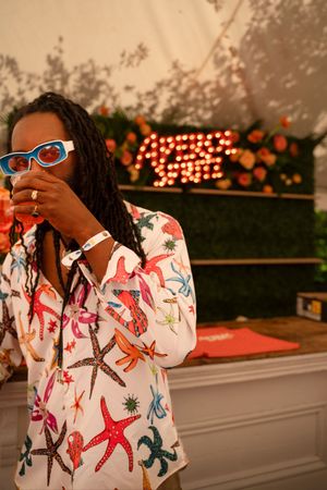 Woman in colorful starfish-print shirt and blue sunglasses poses at a festive outdoor event with floral decor.