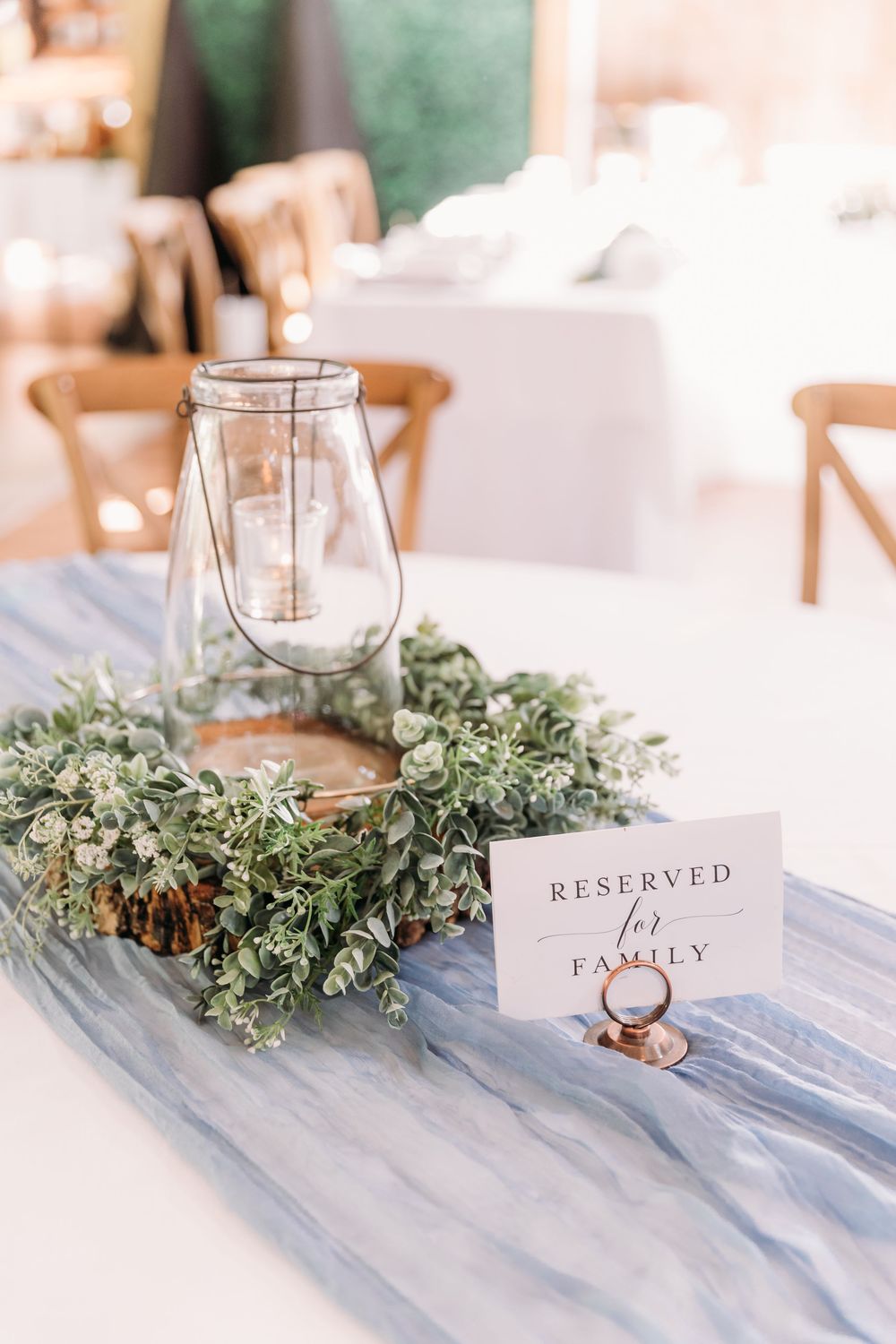 Elegant wedding table with greenery wreath, glass lantern, and reserved for family sign on dusty blue runner.
