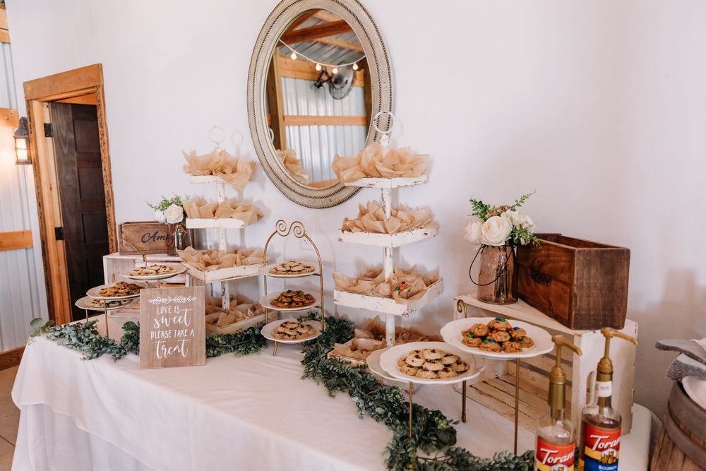Elegant wedding dessert table with tiered stands, assorted pastries, and greenery garland on white linen.