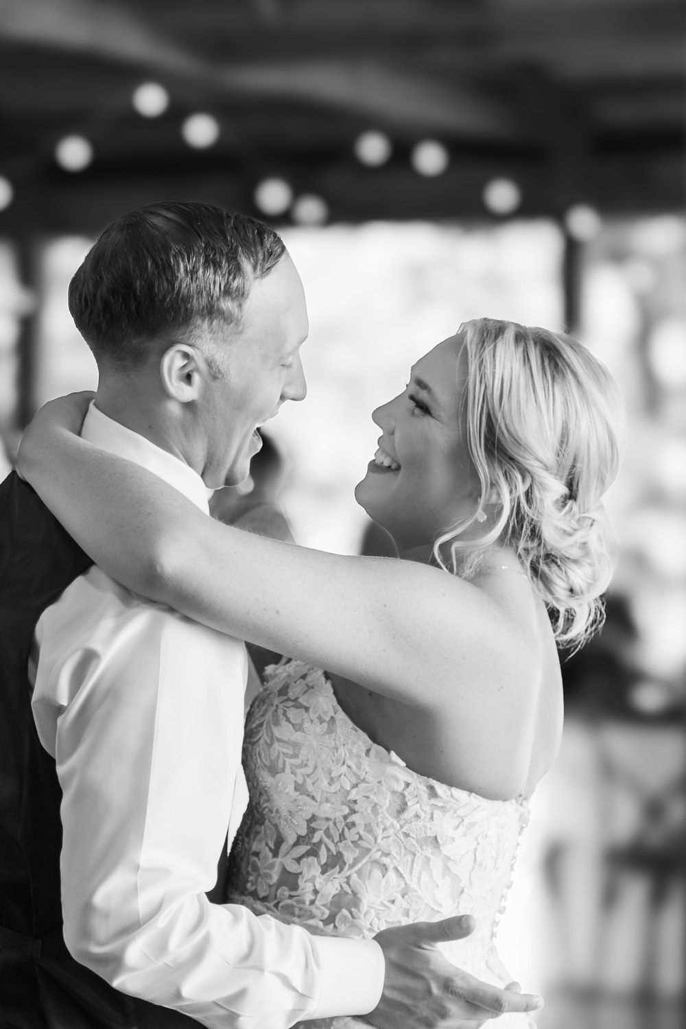 Black and white photo of a laughing bride and groom sharing their first dance at a wedding reception.
