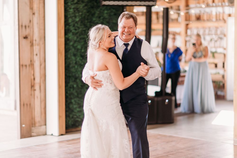 Smiling bride dances with a guest in a rustic barn wedding reception venue with wooden beams and decor.