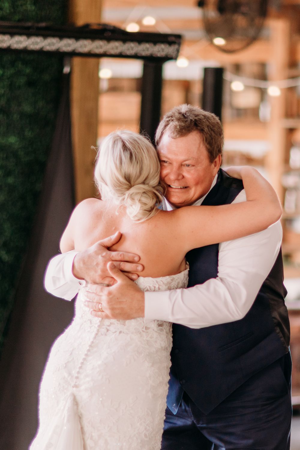 Bride and father sharing an emotional hug during father-daughter dance at rustic barn wedding reception.