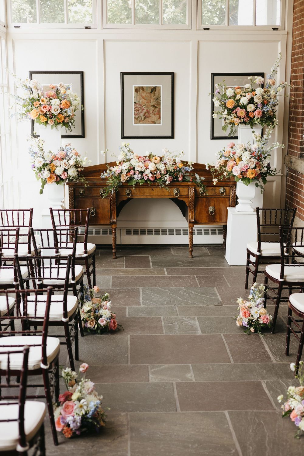 Elegant wedding ceremony backdrop with colourful floral arrangements on antique wooden hutch in the conservatory at Langdon Hall
