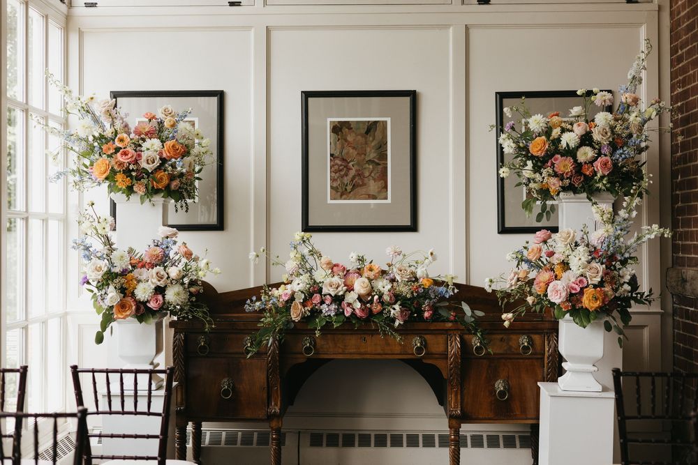 Elegant wedding ceremony backdrop with colourful floral arrangements on antique wooden hutch in the conservatory at Langdon Hall