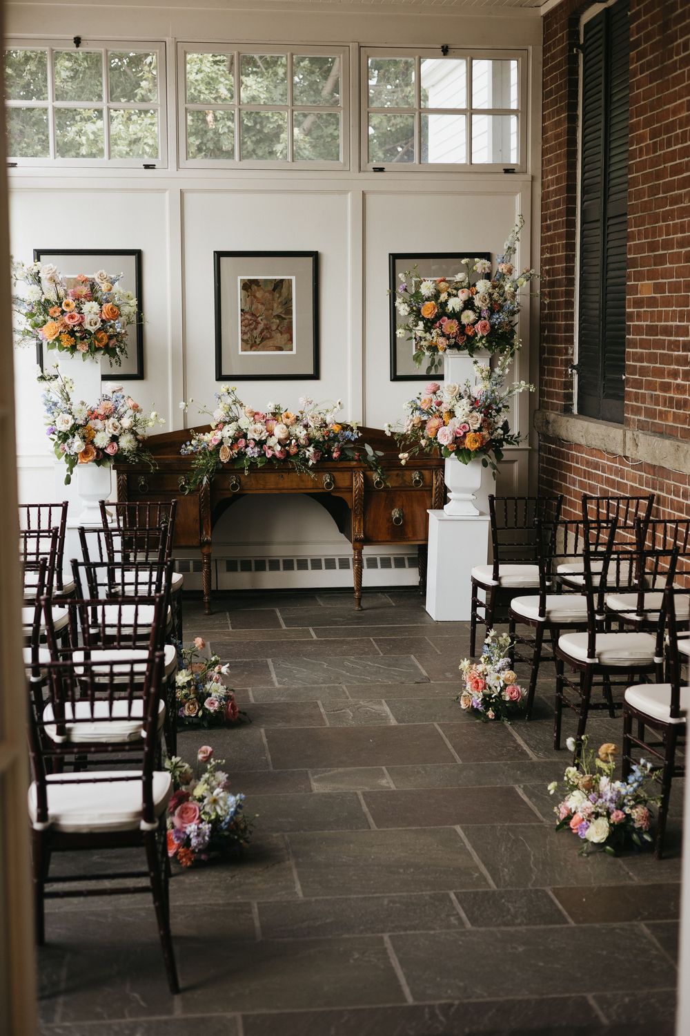 Elegant wedding ceremony setup with colourful floral arrangements on pedestals and chairs lining a stone aisle.