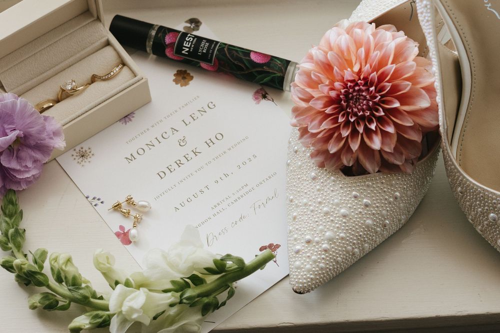 Wedding flat lay featuring invitation for a Bride and Groom at Langdon Hall, pearl heels, flowers, and mascara.
