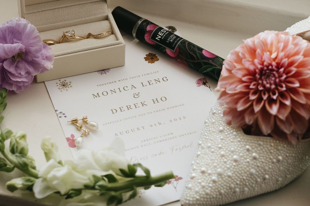 Elegant wedding invitation displayed with gold earrings, pearl clutch, pink dahlia, and luxury pen.