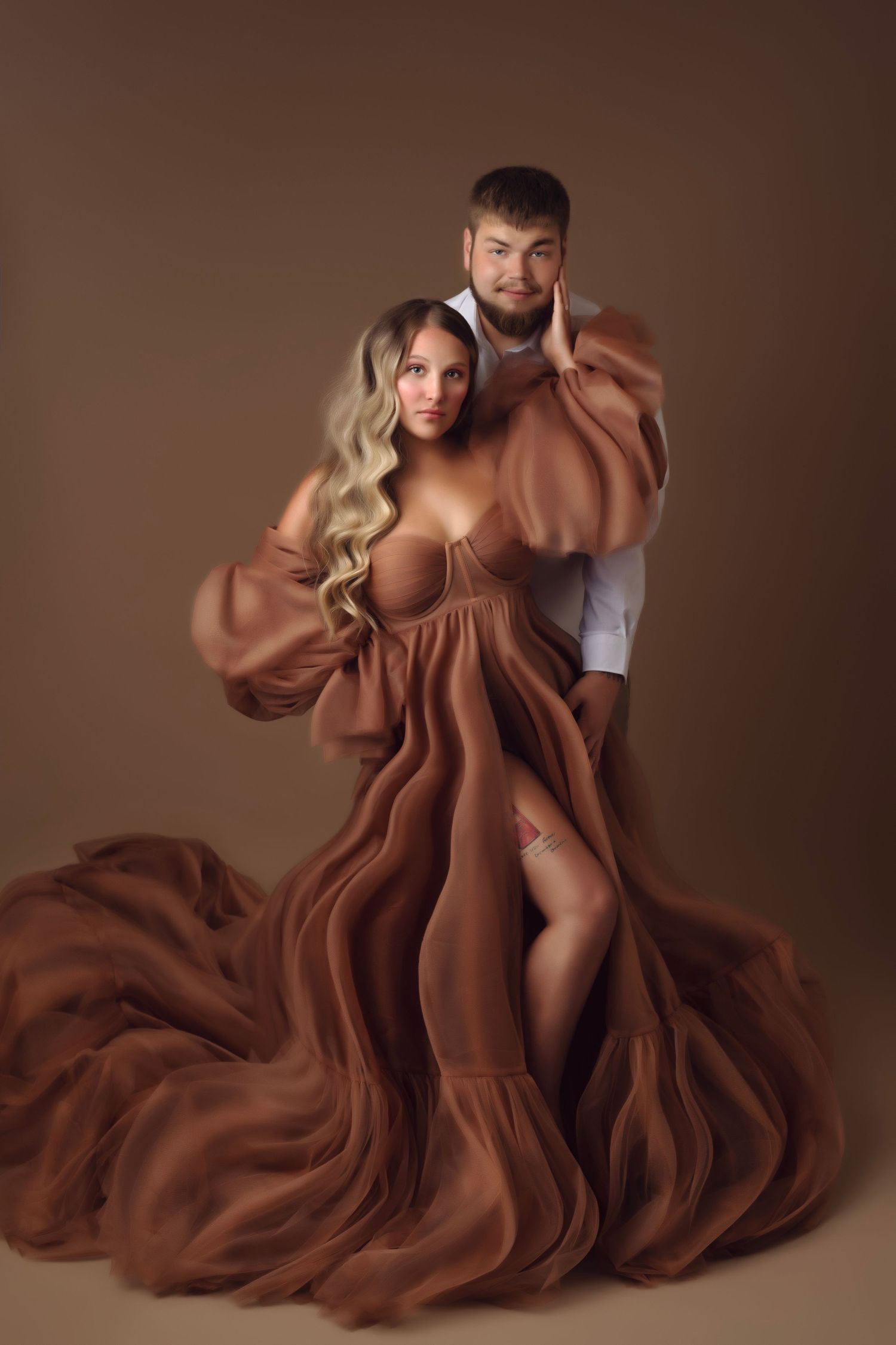 Artistic maternity photos with flowing brown gown against studio backdrop.