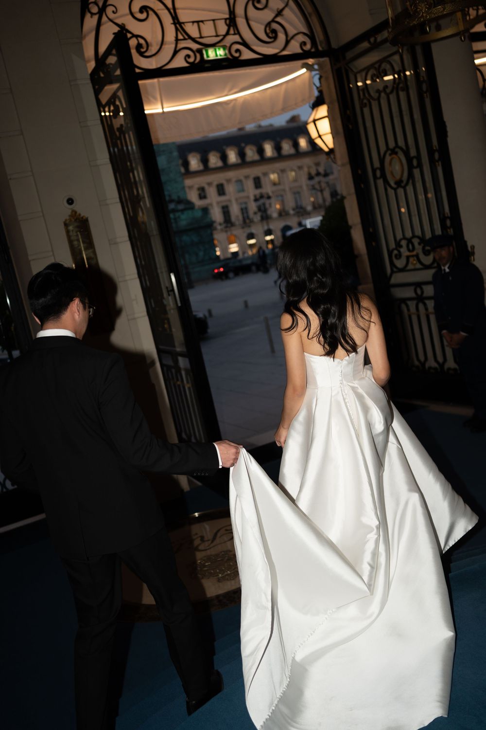 Bride in white gown and groom in black suit walk hand-in-hand through ornate iron gates at elegant wedding venue.